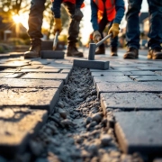 Wegwerkers leggen grijze bestratingstegels op Nederlandse woonstraat, dragen oranje veiligheidsvesten