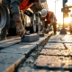 Bouwvakkers leggen grijze betonnen straatstenen op Nederlandse weg, arbeider met oranje vest gebruikt rubberen hamer