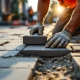 Bouwvakker in oranje veiligheidsvest legt grijze betonklinkers voor stoep, gebruikt rubberen hamer om stenen te nivelleren