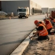 Arbeiders in oranje veiligheidsvesten afwerken betonrand van nieuw geasfalteerde toegangsweg naar logistiek magazijn in Nederland.