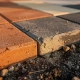 Bestratingssteenmonsters in terracotta, antraciet en zandbeige naast elkaar op verdicht grind, één vervaagd door zon en weer.
