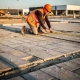 Inspecteur in oranje veiligheidsvest meet betonklinkers op nieuw aangelegde parkeerplaats bedrijventerrein, late middagzon.