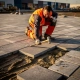 Vakman in oranje veiligheidsvest legt betonnen industriële klinkers op zandbed bij bedrijventerrein, rubberen hamer in hand.