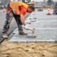 Vakman in oranje veiligheidsvest legt betonklinkers op zandbed bij parkeerterreinaanleg, rubber hamer mid-swing, ooghoogte perspectief.