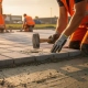 Arbeiders leggen grijze betonklinkers op een parkeerterrein, rubberen hamer in beweging, oranje veiligheidsvesten in goudkleurig avondlicht.