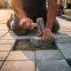 Vakman die met rubberen hamer een grijze betonklinker in een zandbed op een Nederlandse straat plaatst bij gouden uursbelichting.