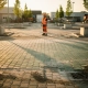 Arbeider in oranje veiligheidsvest inspecteert nieuw aangelegd industrieterrein met waterdoorlatende betonklinkers in Nederland.