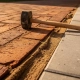 Terracotta klinkers grenzen aan grijze betonnen tegels op een Nederlandse straat, met zand in de voegen en een rubberen hamer op het oppervlak.