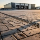 Nieuw bedrijventerrein met betonklinkers en industrieel magazijn op de achtergrond in warm middaglicht.
