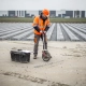 Medewerker in oranje veiligheidsvest meet nieuw geasfalteerd parkeerterrein met meetwiel op Nederlandse bouwplaats.