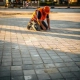 Bouwvakker in oranje veiligheidsvest inspecteert nieuw aangelegd betonnen parkeervak bij laagstaande zon.