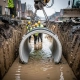 Arbeiders in gele veiligheidsvesten plaatsen een betonnen afvoerpijp in een modderige, waterrijke sleuf tijdens Nederlandse straatreconstructie.