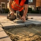 Vakman in oranje veiligheidsvest legt grijze betonklinkers op Nederlandse straat, rubber hamer in beweging, zandbed zichtbaar.